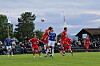 Spillere i røde og blå drakter kjemper om en høy ball på en fotballbane.