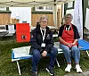 To personer sitter på en feltseng under et telt ved et utendørs arrangement.