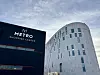 Metro shopping center-skilt på mørk bygning ved siden av en lys, rund bygning under skyet himmel.