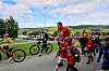 Barn i sykkelhjelmer beveger seg langs en vei med grønne åser i bakgrunnen. Noen går og noen sykler