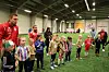 Barn står i rekke på en innendørs fotballbane med trenere og voksne i bakgrunnen.