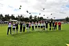 En gruppe mennesker står på en gresskledd fotballbane med ballonger svevende over seg.