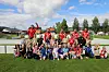 Ungdomsfotballlag i røde drakter samlet til lagbilde på en gressbane.