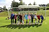 En gruppe barn står på rekke foran et fotballmål på en grønn gressbane.