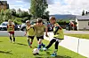Barn i gule vester spiller fotball ved en hvit kant på en gressbane.