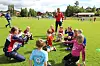 Barn sitter i sirkel på en fotballbane mens en trener står i nærheten.