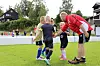 Barn og trener samlet på en gressbane under en fotballøvelse.