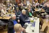 En gruppe eldre mennesker sitter ved bord i et innendørs møtelokale.