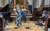 Flere musikere står og sitter foran alteret i en kirke med piano, gitar og mikrofoner.