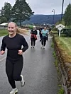 Flere personer jogger på en våt vei med åser og trær i bakgrunnen.