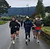 Flere løpere jogger på en våt vei med fjellandskap i bakgrunnen.