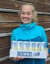 Smilende jente i blå jakke holder en eske med NOCCO-drikker.