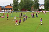 Barn spiller fotball på en grønn bane med hus og trær i bakgrunnen.