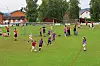 Barn spiller fotball på en grønn bane med hus og trær i bakgrunnen.