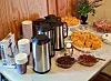 Kaffekanner, pappkopper og fat med bakverk på et dekket buffetbord.