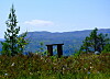 Lite utsiktspunkt med benk foran fjell og skog under klar himmel.
