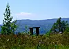 Lite utsiktspunkt med benk foran fjell og skog under klar himmel.
