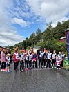 Barn og voksne står samlet på en våt vei før et utendørs løp, med skog og overskyet himmel i bakgrunnen.