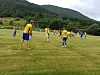 Spillere i gule fotballtrøyer står på en gressbane med fjell og skog bak.