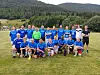 En gruppe personer i blå drakter står og sitter samlet utendørs på en gresslette.