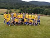 Et fotballag i gule og blå drakter står og kneeler på en gressbane foran skog og åser.
