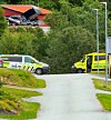 Politi- og ambulansekjøretøy står ved en vei med grøntområde og bygninger i bakgrunnen.