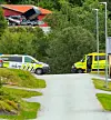 Politi- og ambulansekjøretøy står ved en vei med grøntområde og bygninger i bakgrunnen.
