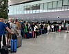 Reisende med kofferter står i kø foran innsjekkingsskranker i en lys flyterminal.