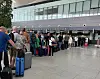 Reisende med kofferter står i kø foran innsjekkingsskranker i en lys flyterminal.