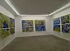 Hvitt gallerirom med flere abstrakte blå og grønne malerier på veggene.