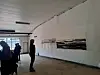 Personer står i et lyst gallerirom og betrakter kunstverk hengt på en hvit vegg.