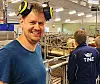 Mann med verneutstyr står i et meieri med Tine-ansatt i bakgrunnen.