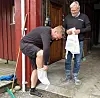To menn ved en rød bygning holder hvite poser eller kluter utenfor en inngang.