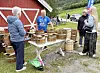 Mennesker står ved bord med trekrus og ølkrus foran en rød låve på landet.