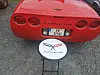 Rød Chevrolet Corvette sett bakfra med Corvette-logo på et lite bord foran bilen.
