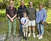 Fire voksne og et barn står sammen på en sti foran grønne busker og trær.
