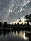Person i silhuett hopper fra stupebrett over vann ved solnedgang.
