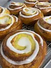 Flere kanelboller med hvit glasur ligger tett på en rist.