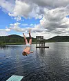Person gjør et baklengs stup i Igltjønna ved en badeplattform under skyet himmel.