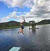 En person gjør en salto bakover fra en brygge ut i vannet ved en innsjø.