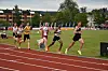 Friidrettsløpere i ulike drakter konkurrerer på en rød løpebane foran tribuner og grønt gress.