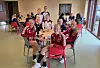 Barn og voksne i håndballdrakter sitter samlet ved små bord i en lys spisesal med røde stoler.