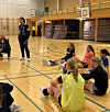 Ungdommer sitter på gulvet i en gymsal mens en instruktør står ved siden av og holder en økt.