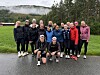 En gruppe står og sitter samlet på en våt vei foran en gressbakke og tåket skog.