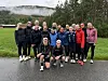 En gruppe står og sitter samlet på en våt vei foran en gressbakke og tåket skog.