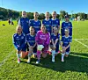 Sju fotballspillere i blå drakter og én i rosa keeperdrakt poserer på en gressbane.