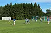 Ungdommer spiller fotball på en gressbane med mål, dommer og skog i bakgrunnen.