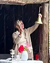 En kvinne ringer med en messingklokke inne i en gapahuk.