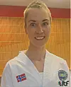Smilende taekwondoutøver i hvit drakt foran en trepanelvegg.