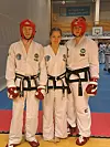 Tre taekwon-do-utøvere i hvite drakter og rødt beskyttelsesutstyr står side om side på en treningsmatte.